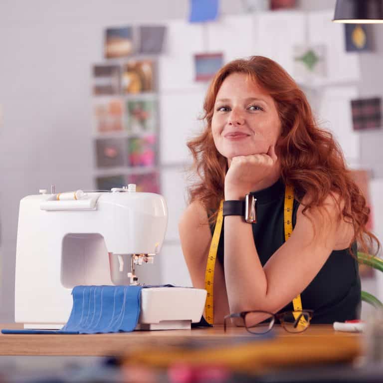 Portrait Of Smiling Female Student Or Business Owner Working In Fashion Using Sewing Machine